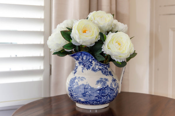 The Fairfield faux floral arrangement of seven large cream Peonies in full bloom in blue and white jug on a wooden table.