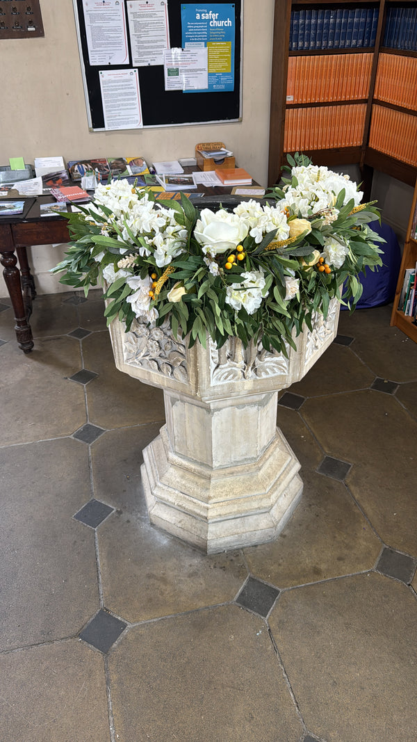 A large faux floral font garland installation for the Church of the Ascension Blackheath, consisting of ivory Hydrangeas, Cream Peonies, Wax flower, yellow Veronica, Ivory Chrysanthemum, Wheat ear stems, Dusted Eucalyptus, Autumn golden Ball Berries, ivory Roses, Ruscus and yellow dried Peony buds. 
arranged in a semi circle on a wreath base bowl on top of the font. 