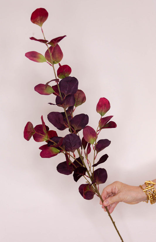A  long stem of artificial Eucalyptus Silver Dollar red foliage with dark burgundy and purple oval leaves.