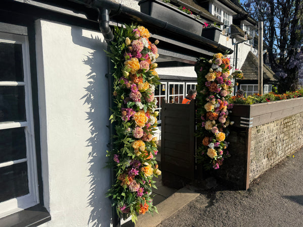 Summer faux floral installation at The Plough Inn Norwood Green with green ruscus, yellow peonies, pink scabiosas, orange hydrangeas, white chrysanthemums, pink and nude dahlias by the front door 