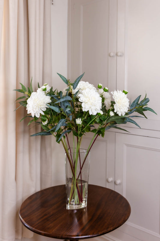 The Austell, a faux floral arrangement, real-touch domed cream with buds,  Eucalyptus Nicolii foliage in a glass vase on a wooden table.